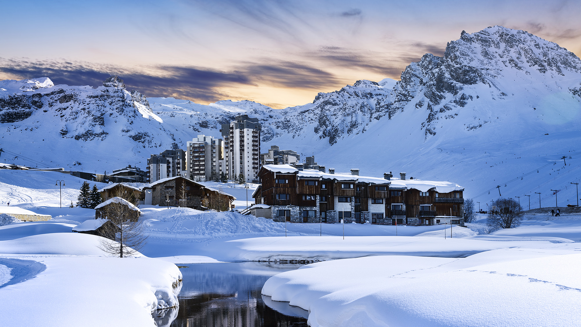 Landscape shot of snow-covered mountains overlooking a small village with a dusky sunset skyline.